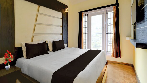 A hotel room with a large bed, a nightstand, a vase with flowers, and a window with curtains. - Super Collection O Hill View Point (Kodaikanal)