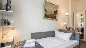 Hotellihuone, jossa on sänky, taulu seinällä, työpöytä tietokoneella ja lamppu.