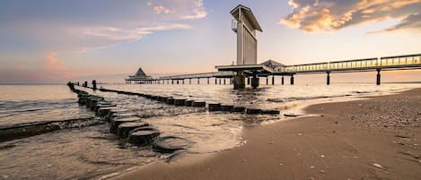 Eine Stegkonstruktion, die ins Wasser ragt, mit einer Aussichtsplattform und einem hohen Gebäude am Ende.