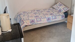 A small, neatly arranged bedroom with a single bed, a bedside table, a nightstand, and a wall-mounted shelf with potted plants. - A friendly budget room that delivers comfort stay (Woolston)