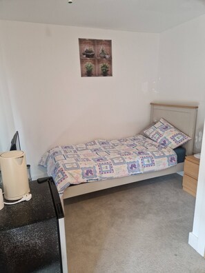 A small, neatly arranged bedroom with a single bed, a bedside table, a nightstand, and a wall-mounted shelf with potted plants. - A friendly budget room that delivers comfort stay (Woolston)