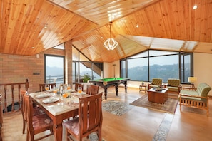 Amplia habitación con mesa de billar, comedor y grandes ventanales con vistas a las montañas.