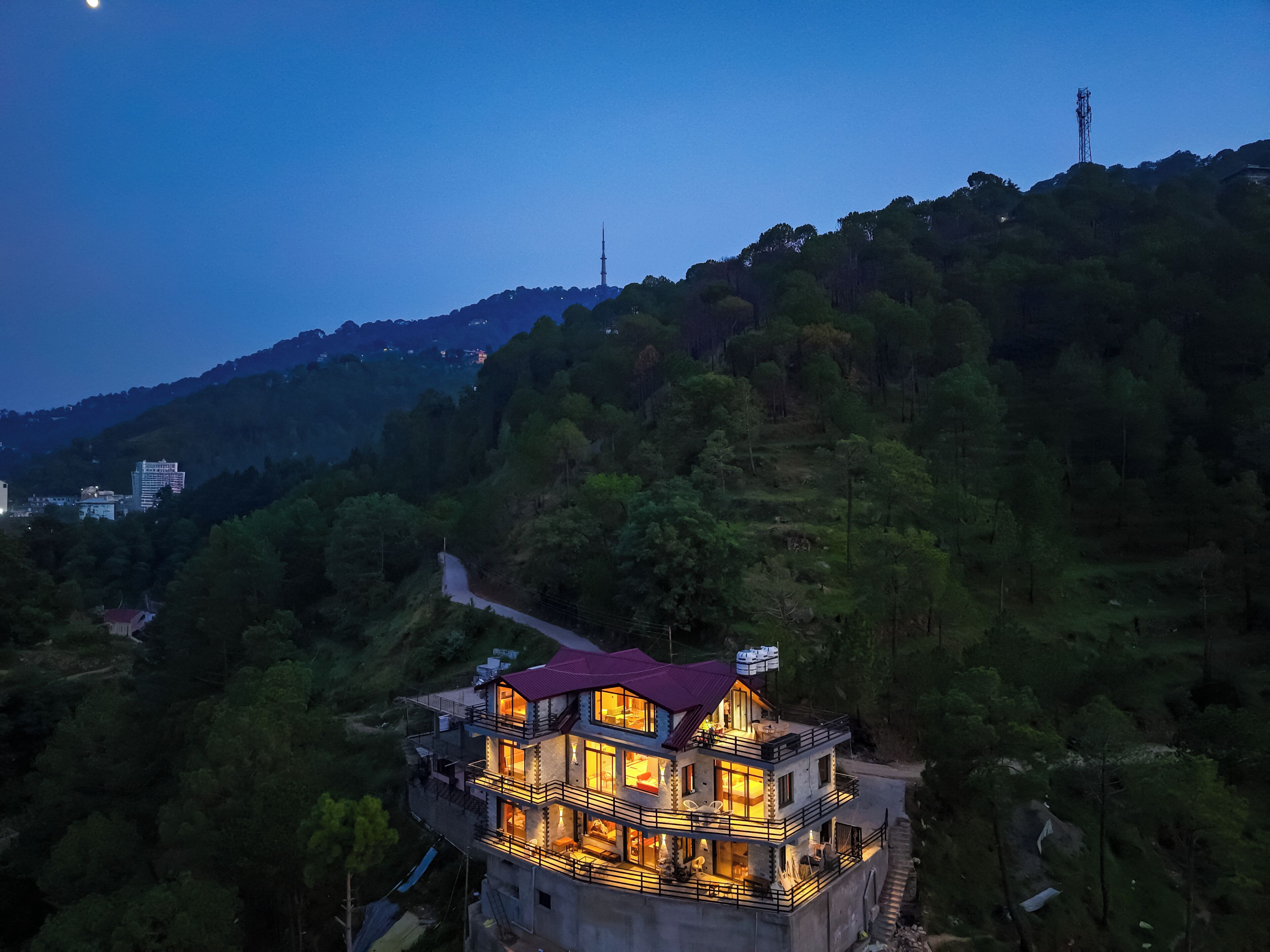 Un edificio de varios pisos con balcones, ubicado en una colina con vistas al bosque circundante y una torre distante.