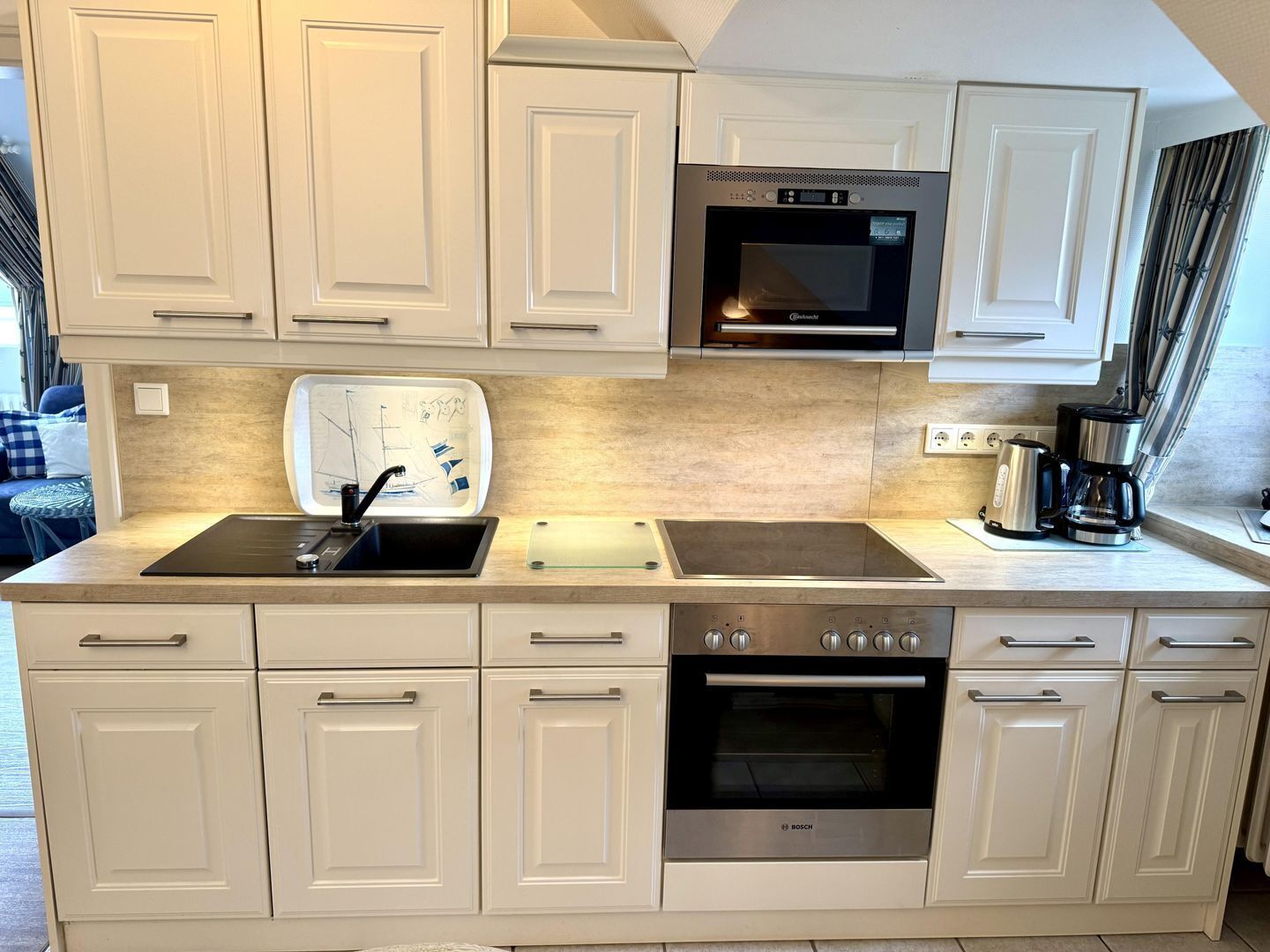 A kitchen with white cabinets, a Bosch oven, a coffee maker, and a window with a view.