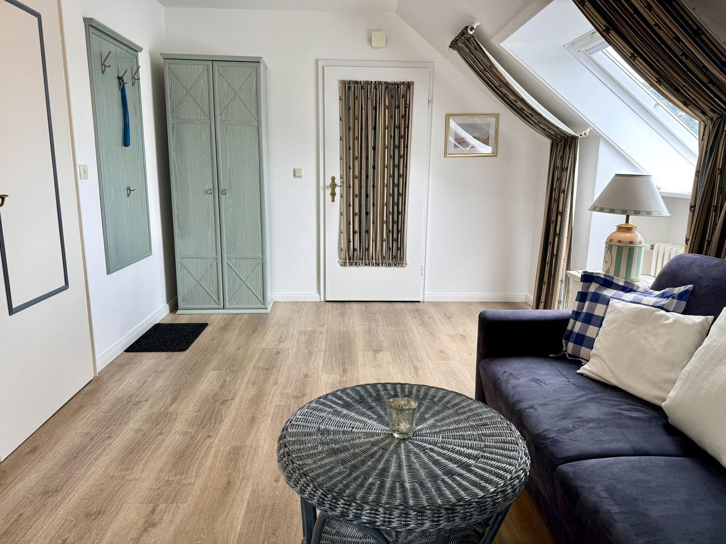 Une pièce avec un canapé bleu foncé, une table ronde en osier et une porte avec un rideau.