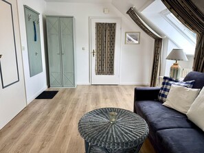 A room with a dark blue sofa, a round wicker table, and a door with a curtain. - Puan-Stöven-Weg, Apartment 1 - Cozy 4-room vacation apartment for 4 people, (Sylt)