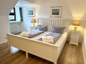 A bedroom with a bed, two bedside tables, a radiator, and two framed pictures on the wall. - Puan-Stöven-Weg, Apartment 1 - Cozy 4-room vacation apartment for 4 people, (Sylt)