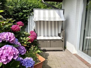 Ein kleiner Außenbereich zum Sitzen mit einem Streifen-Jalousie, umgeben von Topfpflanzen und Blumen.