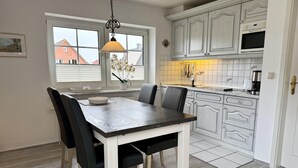 A modern kitchen with white cabinetry, a wooden dining table, and a pendant light. - Kampstraße, Apartment 3a - Cozy 3-room vacation apartment with a balcony in a quiet (Sylt)