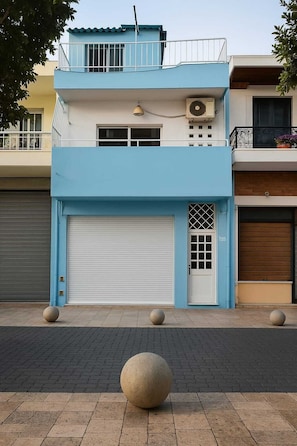 Un edificio de dos pisos con fachada azul, una puerta de garaje cerrada y un pequeño balcón con barandilla.