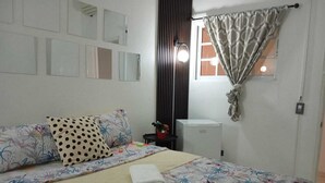 Une chambre à coucher comprenant un lit, une table de chevet, un miroir, une fenêtre avec des rideaux et un luminaire fixé au mur.