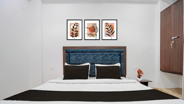 A bedroom with a bed, a headboard, a nightstand, a wall-mounted cabinet, and three framed artworks above the bed. - Collection O Shri Khatu Shyam Ji Temple (Danta Ramgarh)
