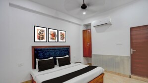 A bedroom with a bed, a wooden wardrobe, an air conditioning unit, and three framed artworks on the wall. - Collection O Shri Khatu Shyam Ji Temple (Danta Ramgarh)