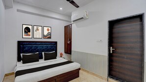 A bedroom with a bed, a ceiling fan, an air conditioning unit, a door, and framed artwork on the wall. - Collection O Shri Khatu Shyam Ji Temple (Danta Ramgarh)