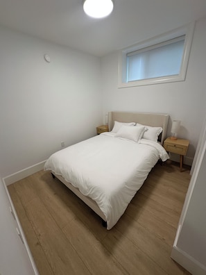 A bedroom with a bed, bedside tables, a window, and a ceiling light. - Cozy Burnaby Heights Suite Private 1BR + 1 Bath (Burnaby)