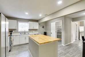 A modern kitchen with white cabinets, a wooden island, and a window with blinds. - 6BR House w/ Massive Parking, Centrally Located (Houston)
