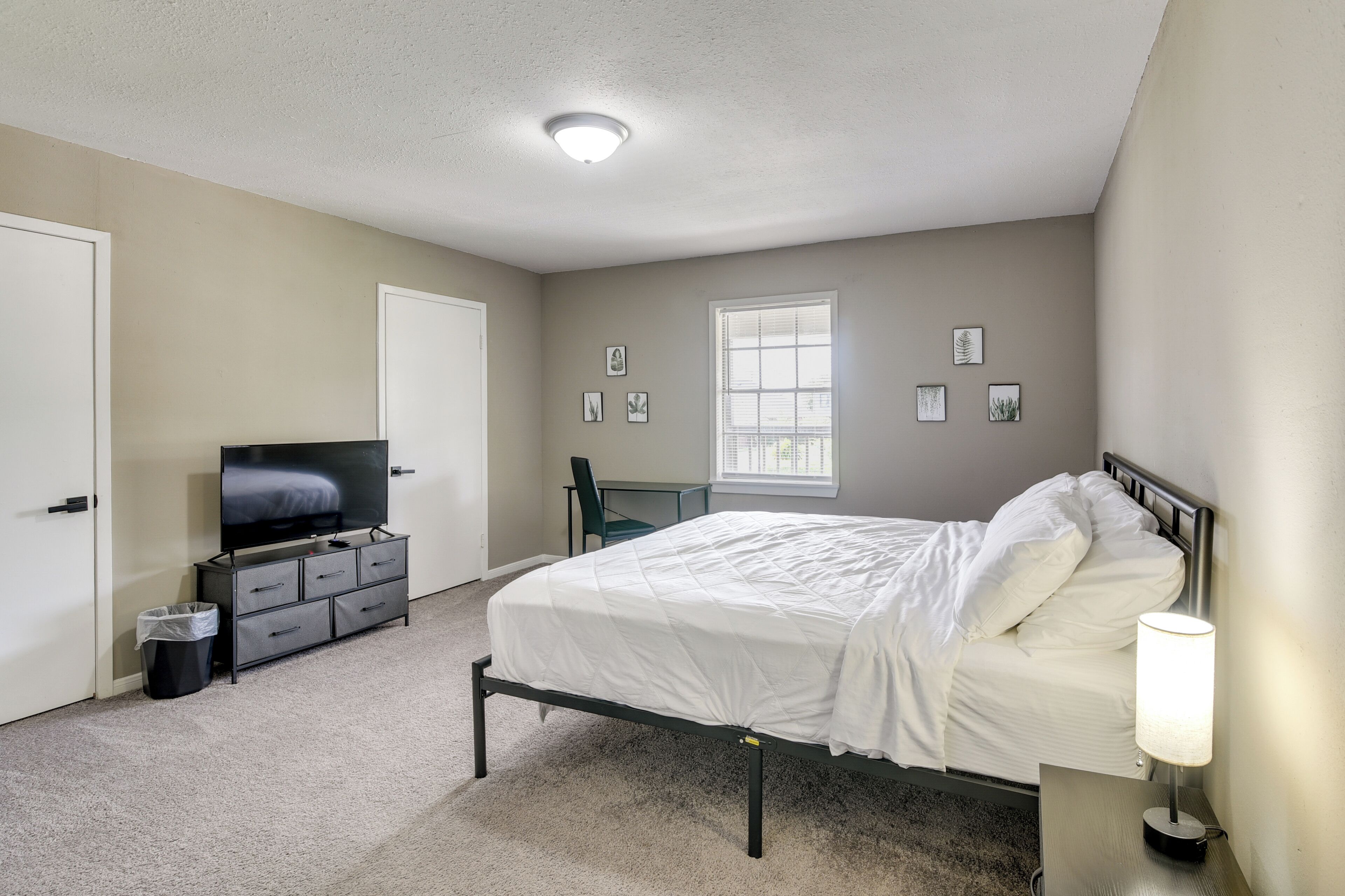 A bedroom with a bed, a TV, a desk, and a window.
