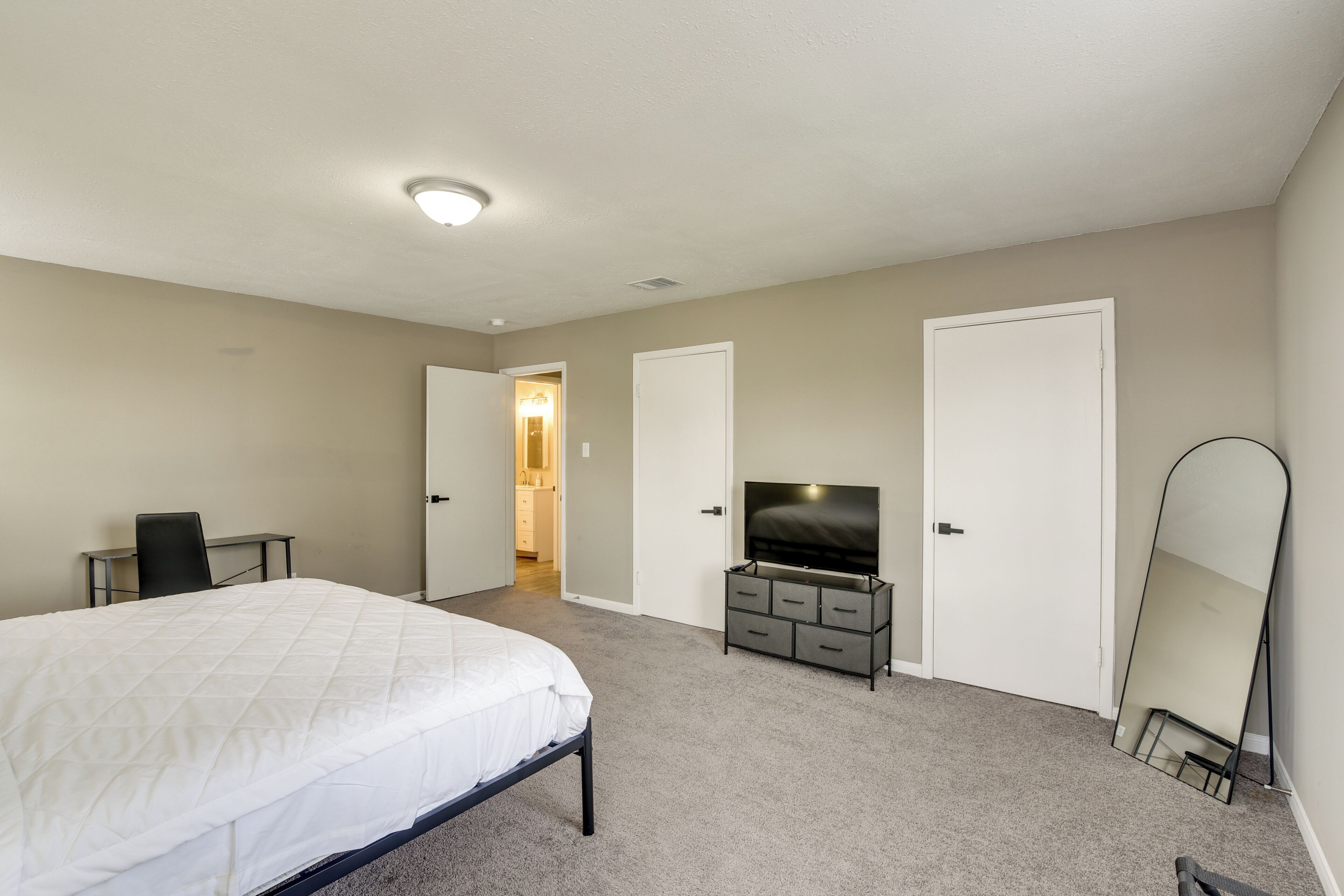 A bedroom with a bed, a TV, a dresser, and a mirror.
