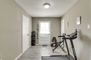 Un pasillo con una cinta de correr, un soporte para pesas y una puerta que da a una habitación.