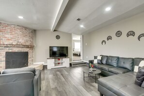 A modern living room with a brick fireplace, a flat-screen TV, a grey sofa, and decorative wall art.