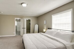 Un dormitorio con cama, lámpara de noche, ventana con persianas y puerta que da a un baño.