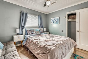 Ein Schlafzimmer mit Bett, Nachttischen, einem Schminktisch, einem Fenster mit Vorhängen, einem Deckenventilator und einer Tür.