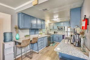 A kitchen with blue cabinets, a water dispenser, a coffee maker, and a fire extinguisher.