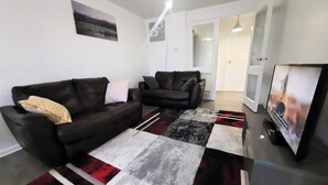 A living room with two black sofas, a patterned rug, and a flat-screen TV. - Joydens Wood, 2-bed Apt, Sleeps 4 With Parking (Grays)