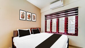 A hotel room with a bed, a window with a red frame, and an air conditioner on the wall. - Collection O Kottayam Formerly Sap Inn (Kottayam)