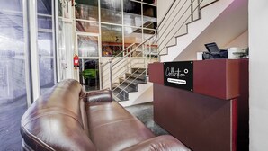 A reception area with a leather couch, a staircase, and a sign indicating company service. - Collection O Kottayam Formerly Sap Inn (Kottayam)