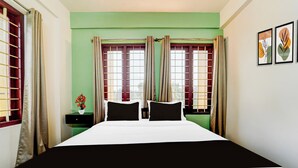 A bedroom with a bed, two nightstands, a vase with flowers, and curtains on the windows. - Collection O Kottayam Formerly Sap Inn (Kottayam)