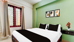 A bedroom with a bed, a window with curtains, a nightstand, and a wall with framed artwork. - Collection O Kottayam Formerly Sap Inn (Kottayam)