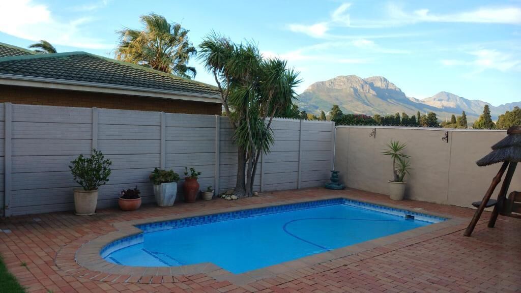 Un jardín trasero con piscina, plantas en macetas y vistas a montañas.