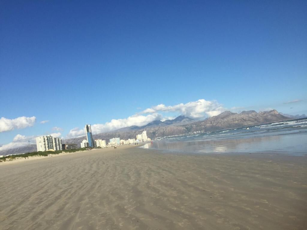 Uma praia com edifícios ao fundo e montanhas à distância.