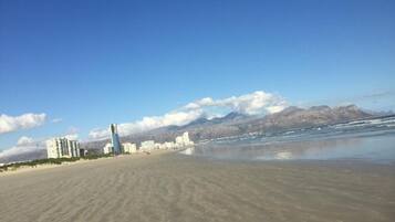 Uma praia com edifícios ao fundo e montanhas à distância.