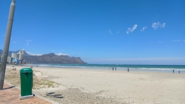 En strand med klart skys og nogle mennesker, samt et bjerg i baggrunden.