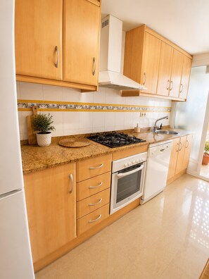 A kitchen with wooden cabinets, a gas stove, a dishwasher, and a tiled backsplash. - Spacious 2BR Pool Parking Near the Beach (Alicante)
