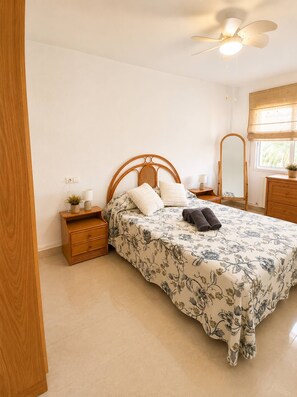 A bedroom with a bed, wooden nightstands, a ceiling fan, a window with a view, and a mirror. - Spacious 2BR Pool Parking Near the Beach (Alicante)