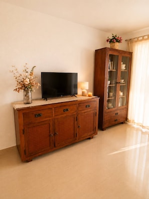 A wooden cabinet with a flat-screen TV, a vase with flowers, and a candle on top. - Spacious 2BR Pool Parking Near the Beach (Alicante)
