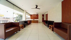 A reception area with a reception desk, seating, ceiling fans, and a view through large windows. - Super Collection O Kottayam (Kottayam)