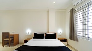 A hotel room with a bed, two bedside tables, a chair, a window with curtains, and an air conditioning unit. - Super Collection O Kottayam (Kottayam)