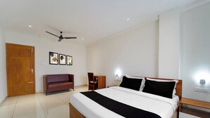 A hotel room with a bed, a sofa, a desk, and a ceiling fan. - Super Collection O Kottayam (Kottayam)