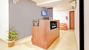 A reception desk with a television mounted on the wall, a fire extinguisher, and a plant. - Collection O Uttaranchal University (Dehradun)