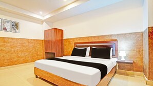 A hotel room with a wooden bed, a nightstand with a lamp, and a wall with framed artwork. - Collection O Uttaranchal University (Dehradun)
