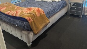 A bedroom with a tufted headboard, a bed with floral bedding, a nightstand with a lamp, and abstract wall art.