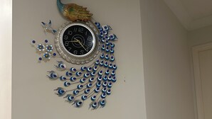 A wall-mounted clock with a peacock design and a decorative bird figure above it.