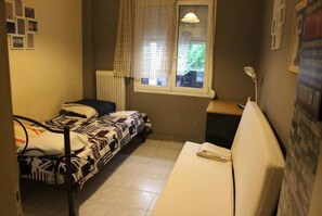Ein kleines Zimmer mit einem Einzelbett, einem Fenster, einer Heizung und einem Nachttisch.