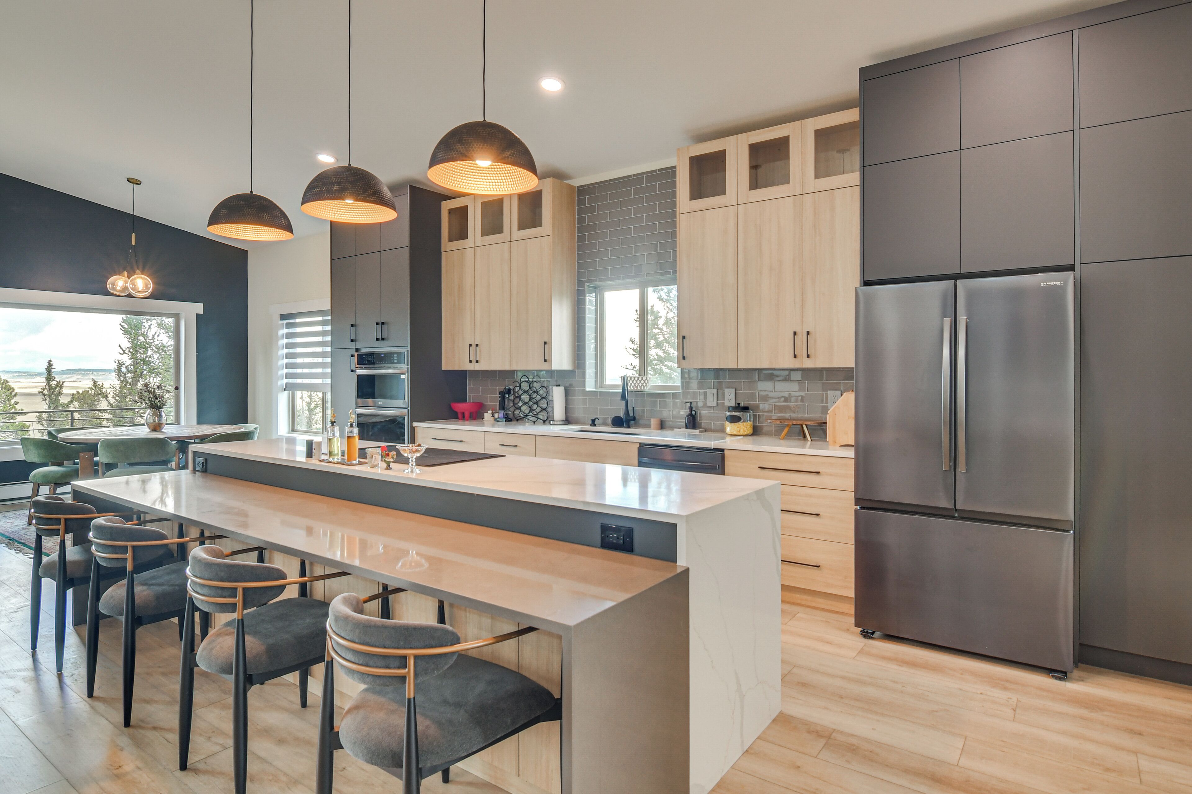 A modern kitchen with a central island, bar stools, stainless steel appliances, and wooden cabinetry.