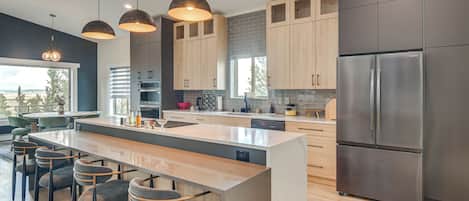 Una cocina moderna con una isla central, taburetes de bar, electrodomésticos de acero inoxidable y armarios de madera.