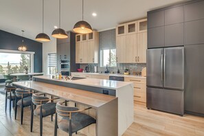 Una cocina moderna con una isla central, taburetes de bar, electrodomésticos de acero inoxidable y armarios de madera.